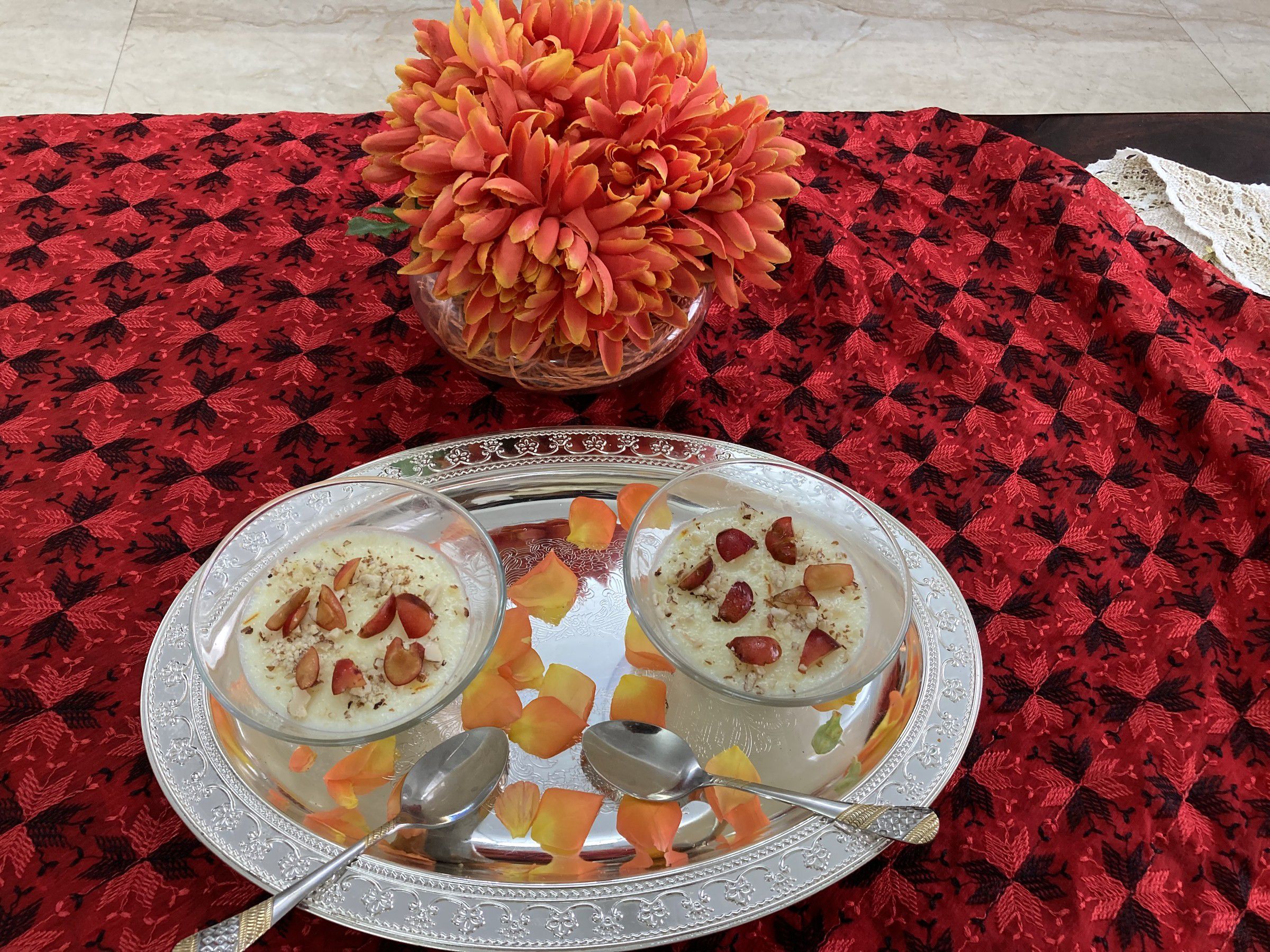 Two glass bowls of a creamy dessert topped with strawberries, on a silver tray scattered with orange petals